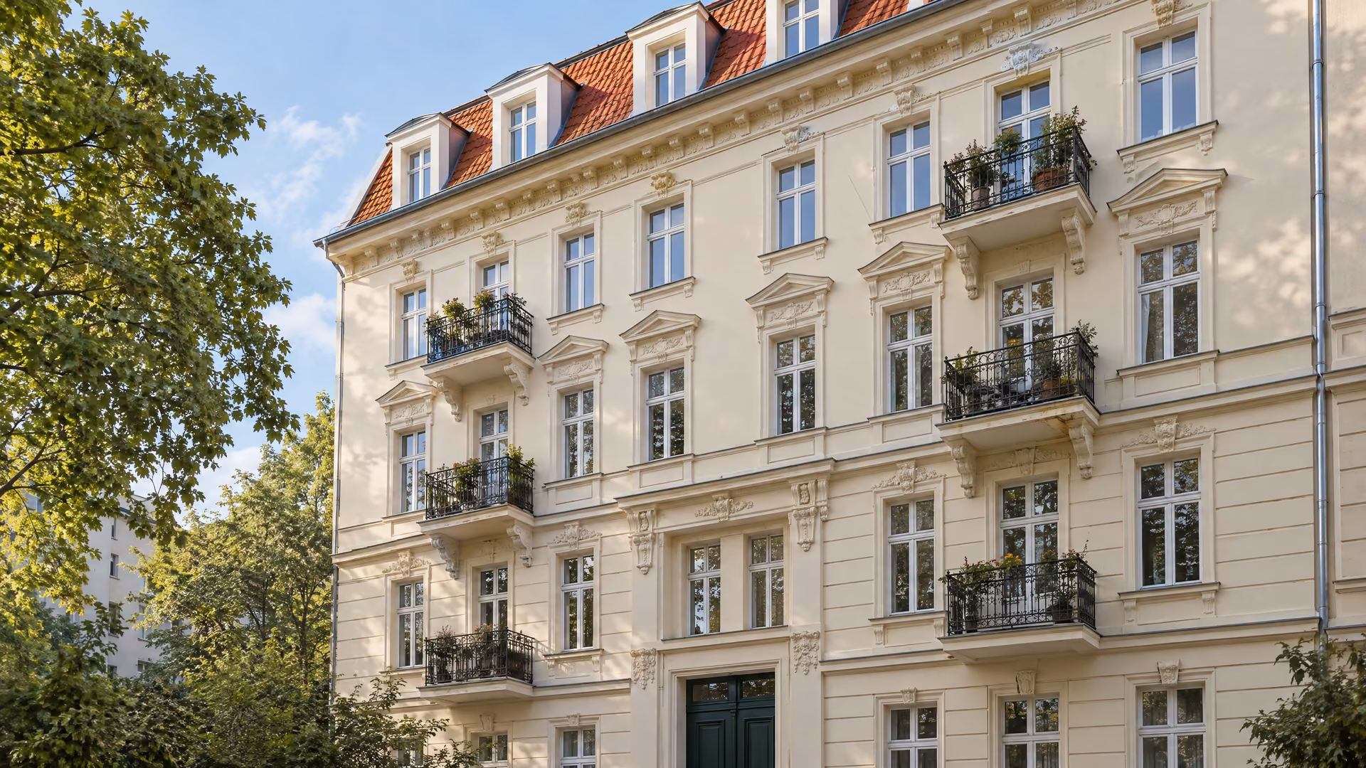 Gepflegtes Berliner Mietshaus aus der Zeit um 1905 mit heller Fassade, Balkonen und rotem Mansarddach.