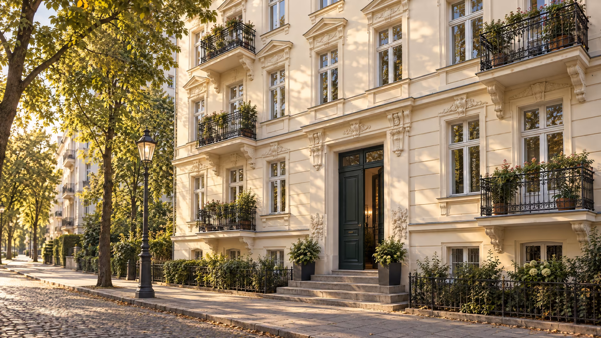 Das Haus im warmen Abendlicht von der Straße aus, mit Haustür, Balkonen und Straßenbäumen.