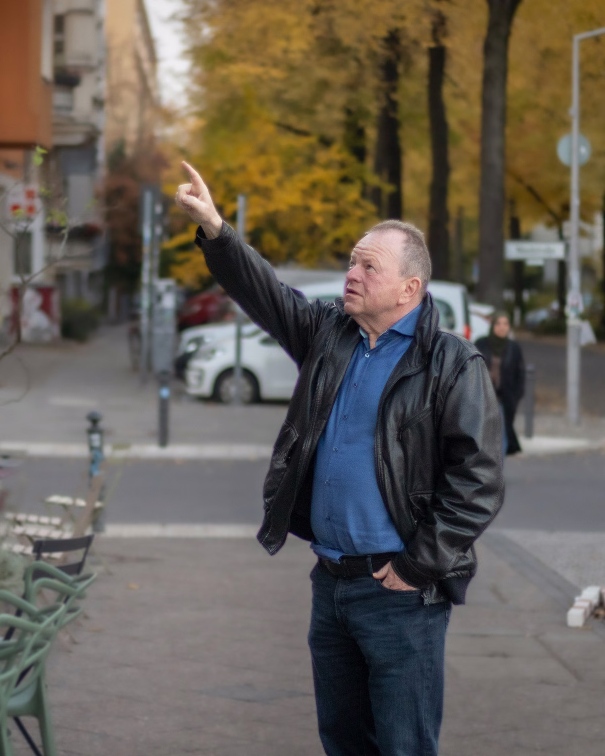 Oliver Preikschat steht auf einer Berliner Straße und zeigt auf ein Wohnhaus gegenüber.
