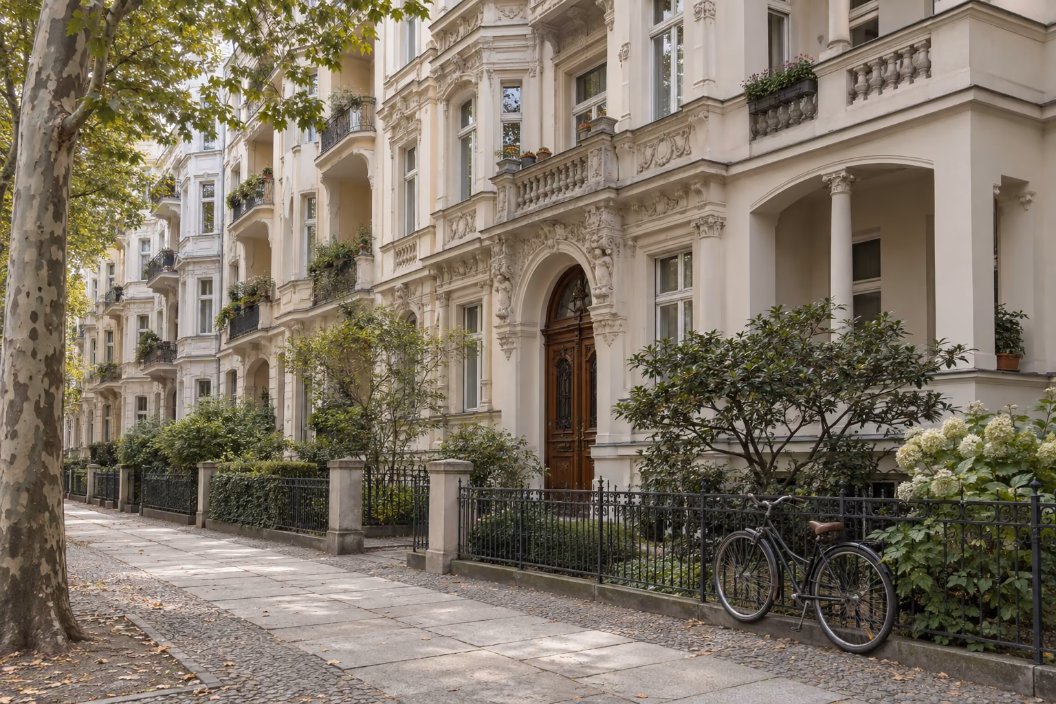 Wohnstraße im Berliner Westen mit hellen Stuckfassaden aus der Zeit um 1905, Vorgärten hinter schmiedeeisernen Zäunen und Platanen am breiten Gehweg. An einem Zaun lehnt ein Fahrrad.