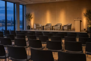 Leerer Veranstaltungssaal am Abend vor einer Podiumsdiskussion. Vor Stuhlreihen steht eine niedrige Bühne mit vier Sesseln und einem Rednerpult.