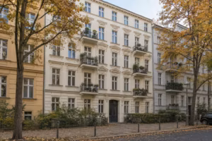 Straßenfront eines fünfgeschossigen Berliner Altbaus mit Stuckfassade und kleinen Balkonen, davor Straßenbäume im Herbst.