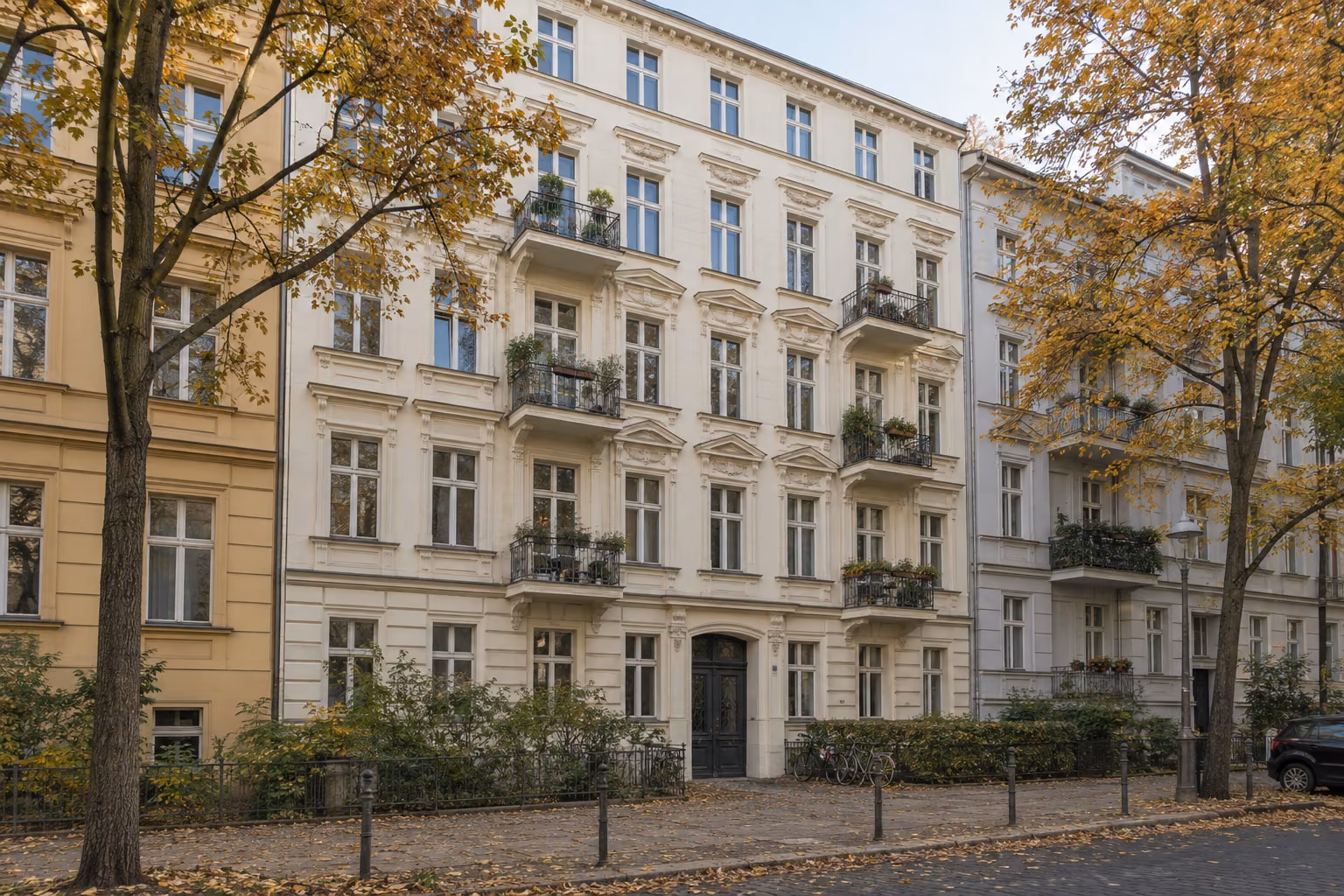 Straßenfront eines fünfgeschossigen Berliner Altbaus mit Stuckfassade und kleinen Balkonen, davor Straßenbäume im Herbst.