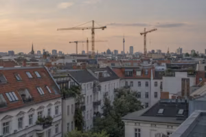 Blick über die Dächer Berliner Altbauten im Abendlicht, dazwischen mehrere Baukräne, am Horizont der Fernsehturm.