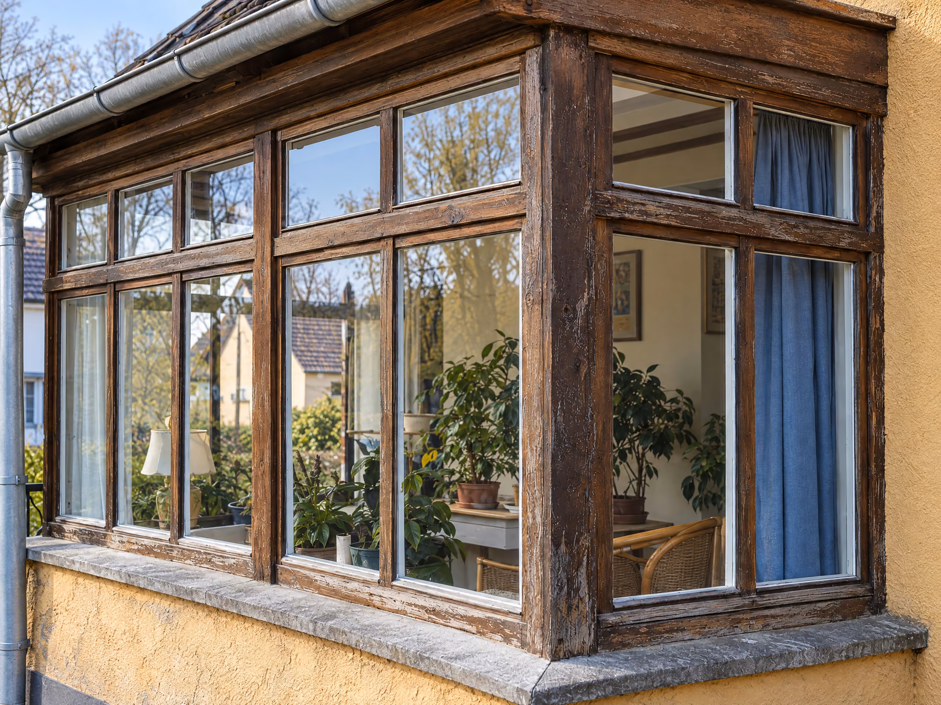 Ältere Holzfenster einer hellen Hausveranda mit sichtbaren Gebrauchsspuren an Rahmen und Fensterbank.