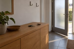 Flur eines Einfamilienhauses: Auf einer Holzkommode liegen zwei getrennte Schlüsselbunde. Die Haustür mit Milchglas steht einen Spalt offen.
