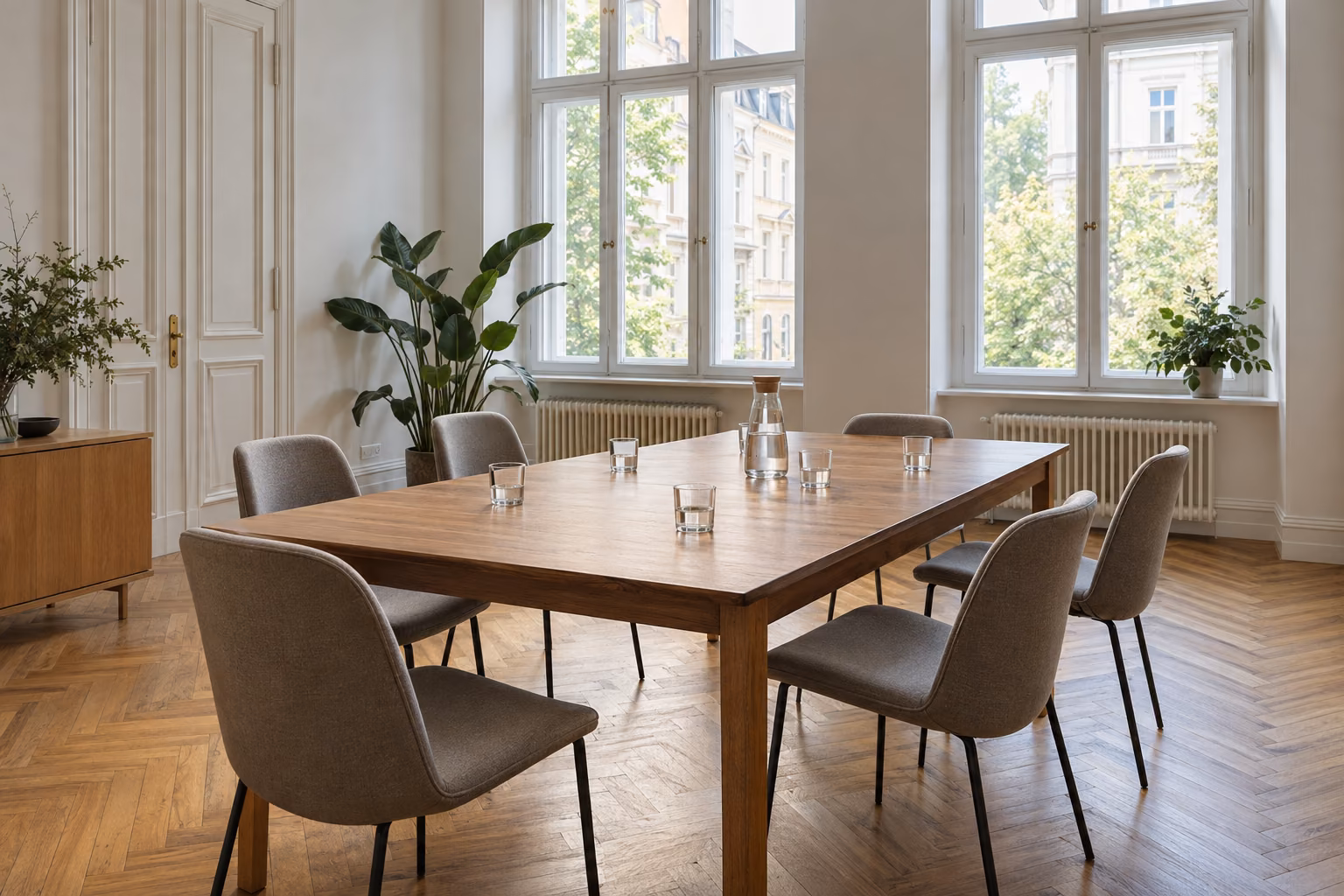 Großer Besprechungstisch mit sechs leeren Stühlen in einem hellen Altbaubüro.