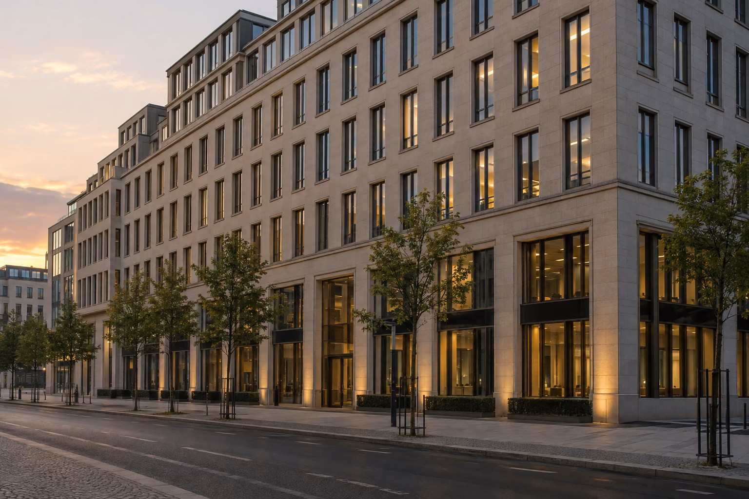 Fassade eines großen Bürohauses mit vielen Fenstern im Abendlicht, davor eine leere Straße.