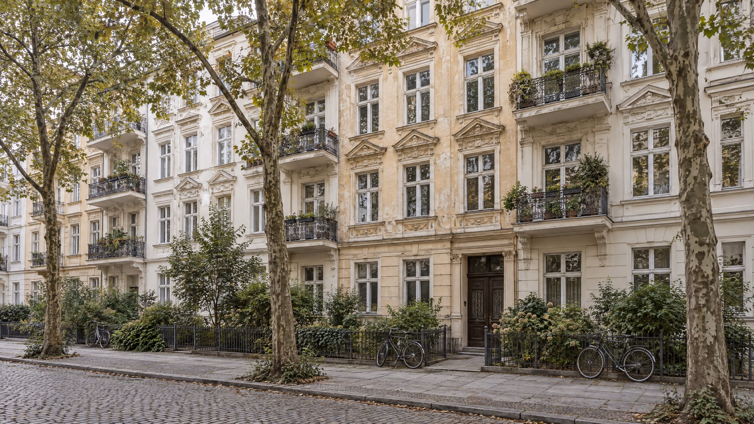 Illustrative Straße in Berlin mit einer Reihe ähnlicher Altbauten aus der Gründerzeit, Balkonen, Platanen und Kopfsteinpflaster.